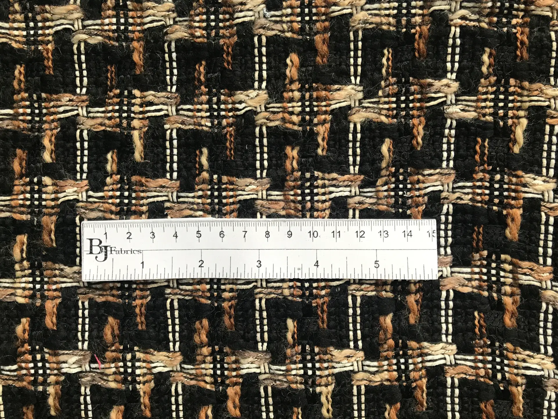 ruler lays on top of black, brown, tan, woven tweed to show scale