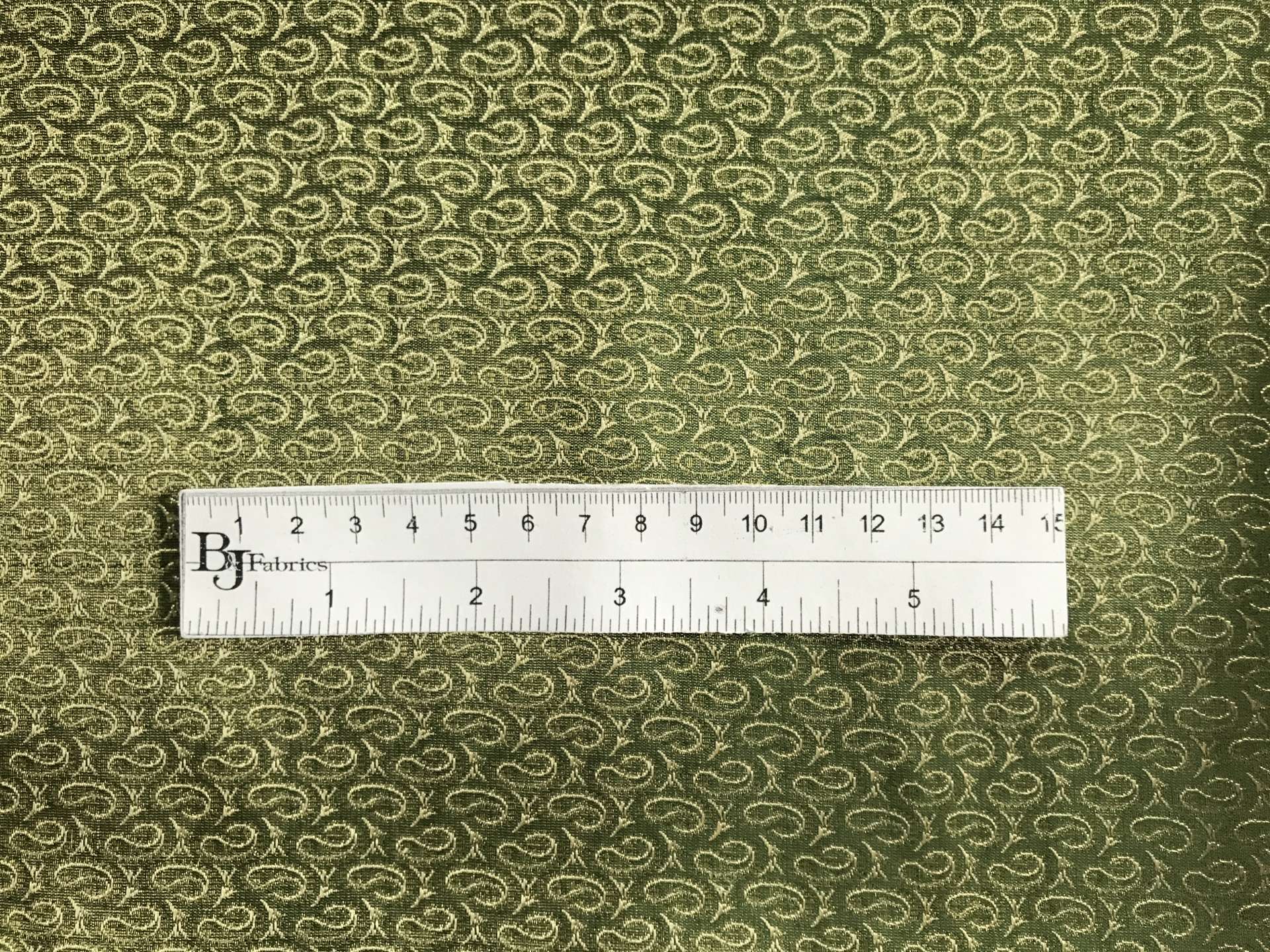 ruler sits on top of metallic green and gold brocade with repeating gold paisleys to show scale of pattern