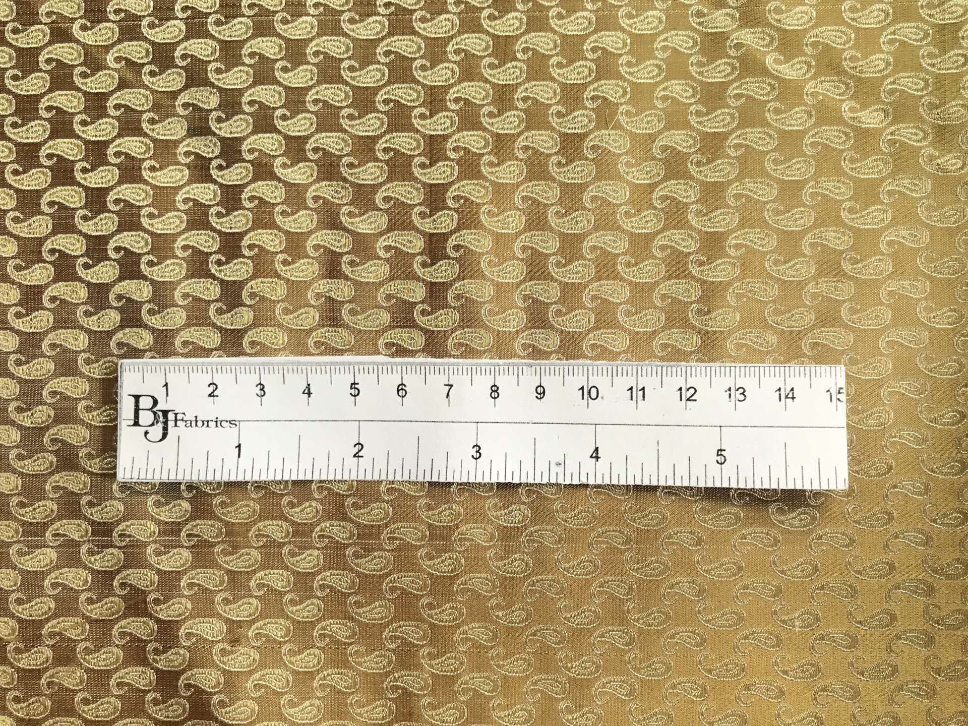 ruler sits on top of gold metallic silk brocade with repeating gold paisleys to show scale of pattern