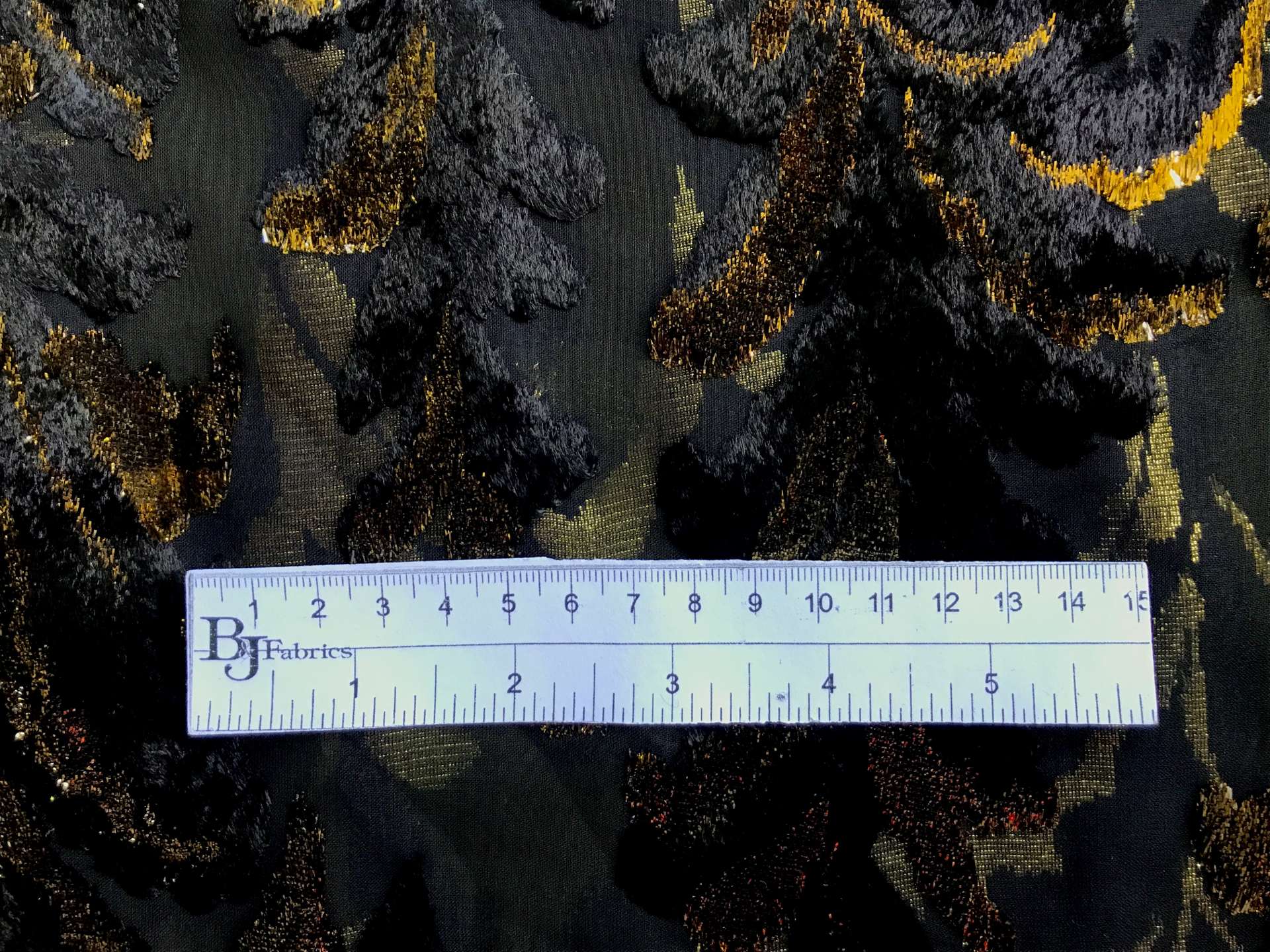 ruler sits on top of black chiffon with burnout velvet in gold lurex in leaves patterns to show scale