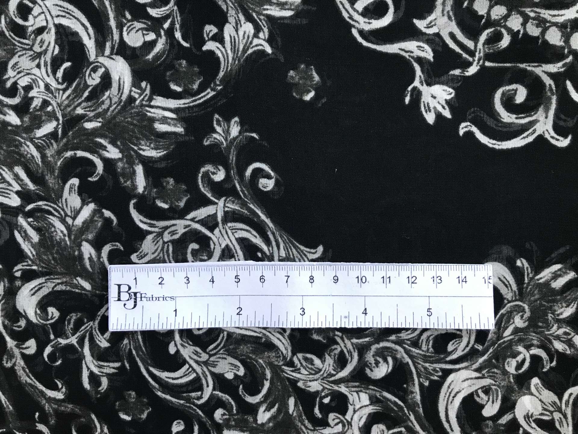 ruler sits on top of printed black chiffon with grey ornamental brocade patterns to show scale of print