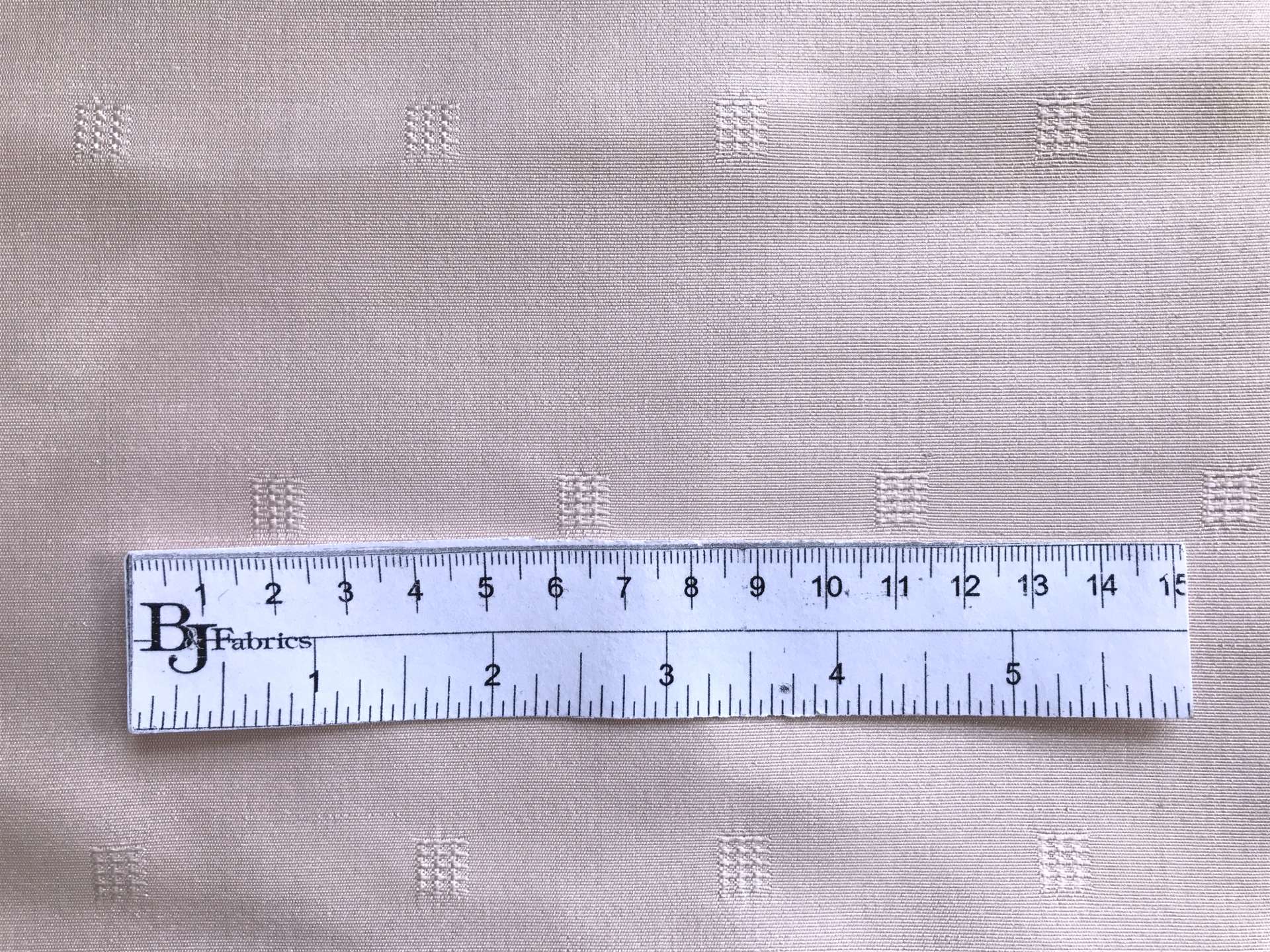 ruler lays on top of blush silk faille with small jacquard squares to show scale of squares