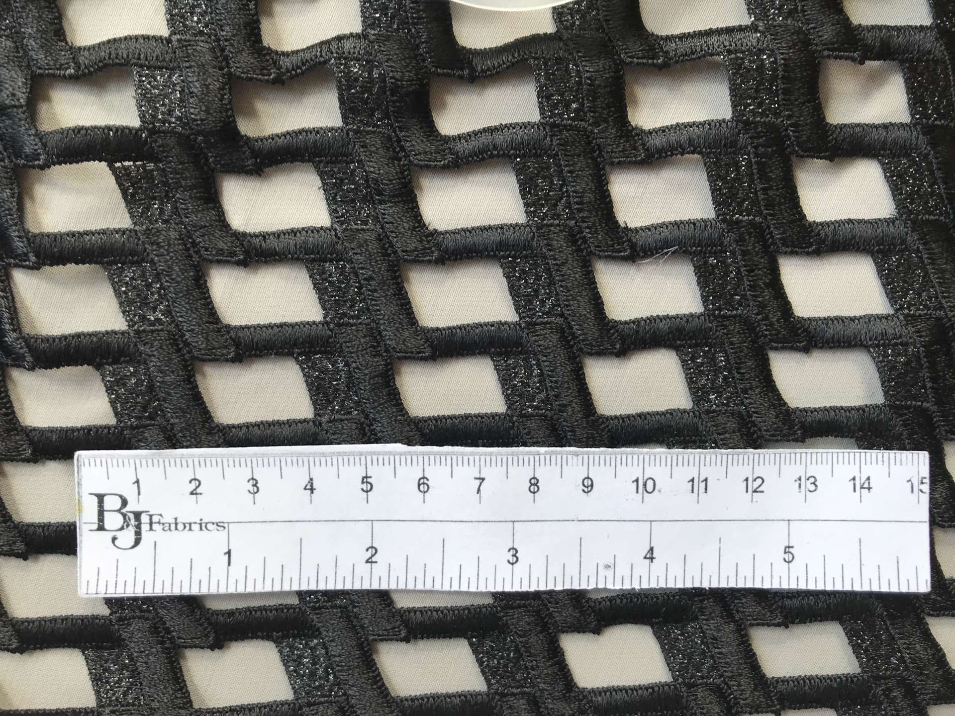ruler sits on top of black metallic guipure lace to show scale of mesh