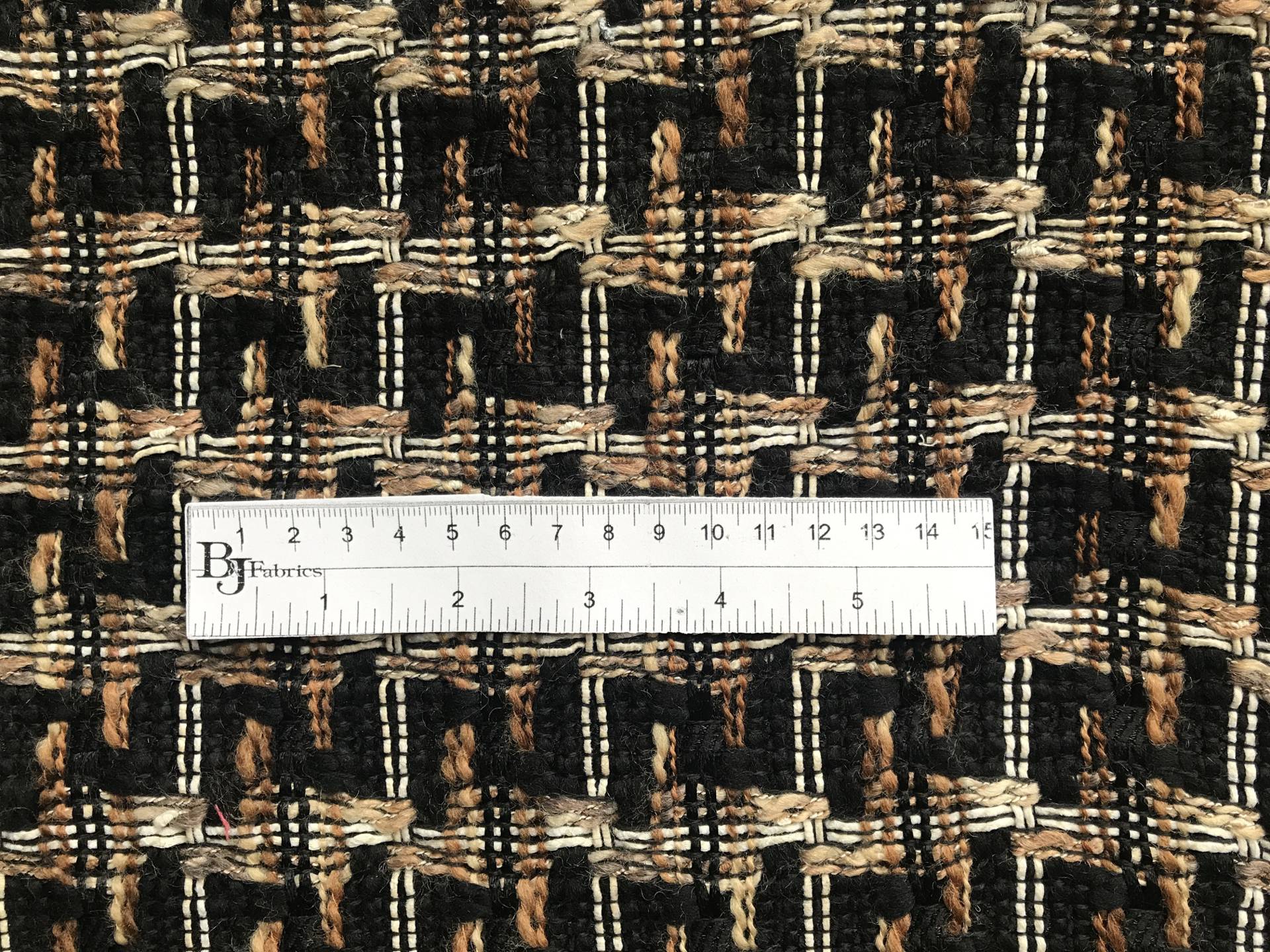 ruler lays on top of black, brown, tan, woven tweed to show scale