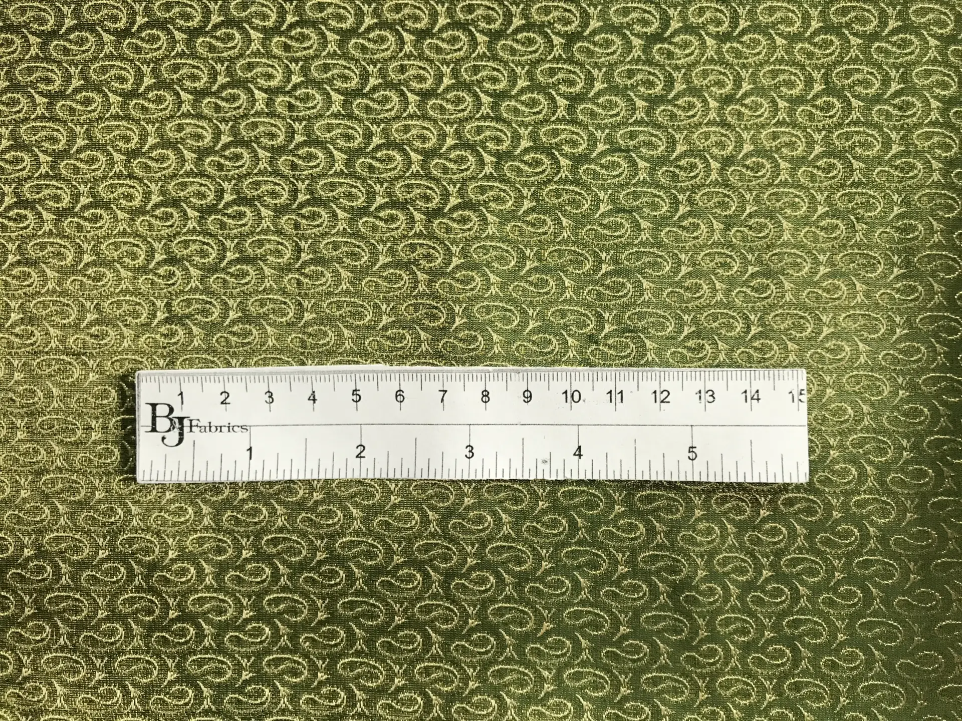 ruler sits on top of metallic green and gold brocade with repeating gold paisleys to show scale of pattern