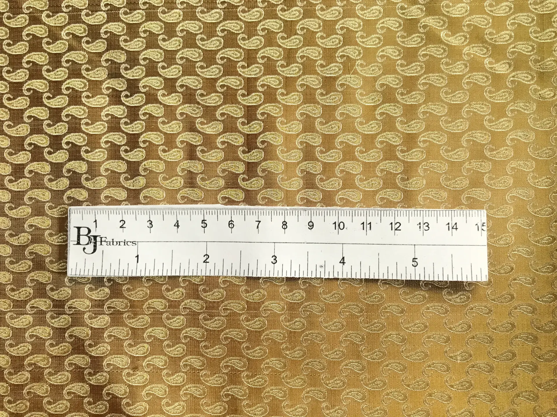 ruler sits on top of gold metallic silk brocade with repeating gold paisleys to show scale of pattern