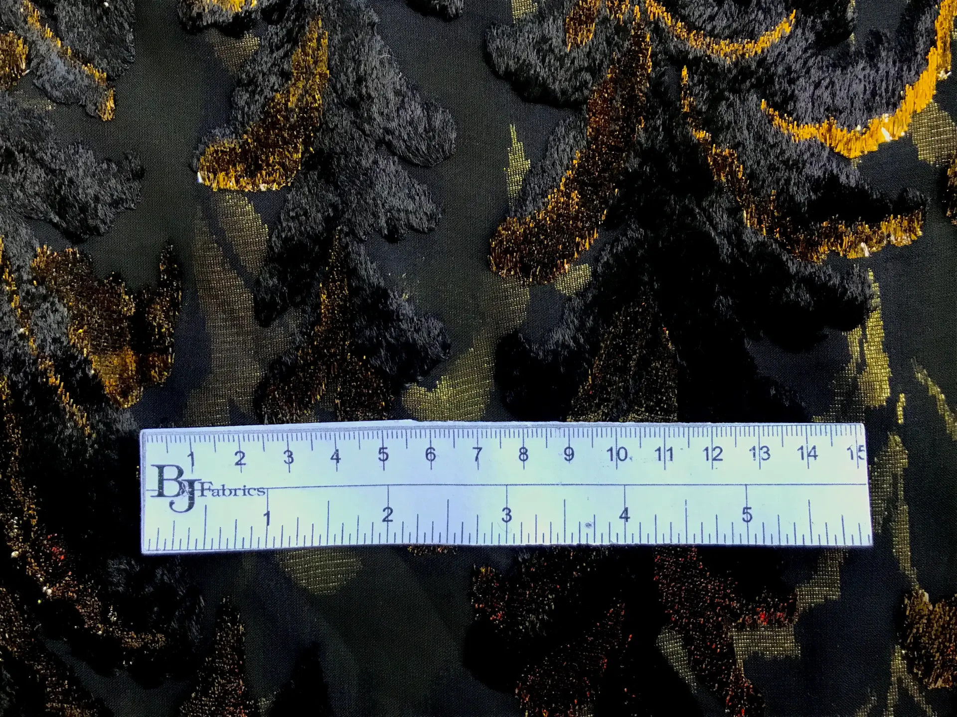 ruler sits on top of black chiffon with burnout velvet in gold lurex in leaves patterns to show scale