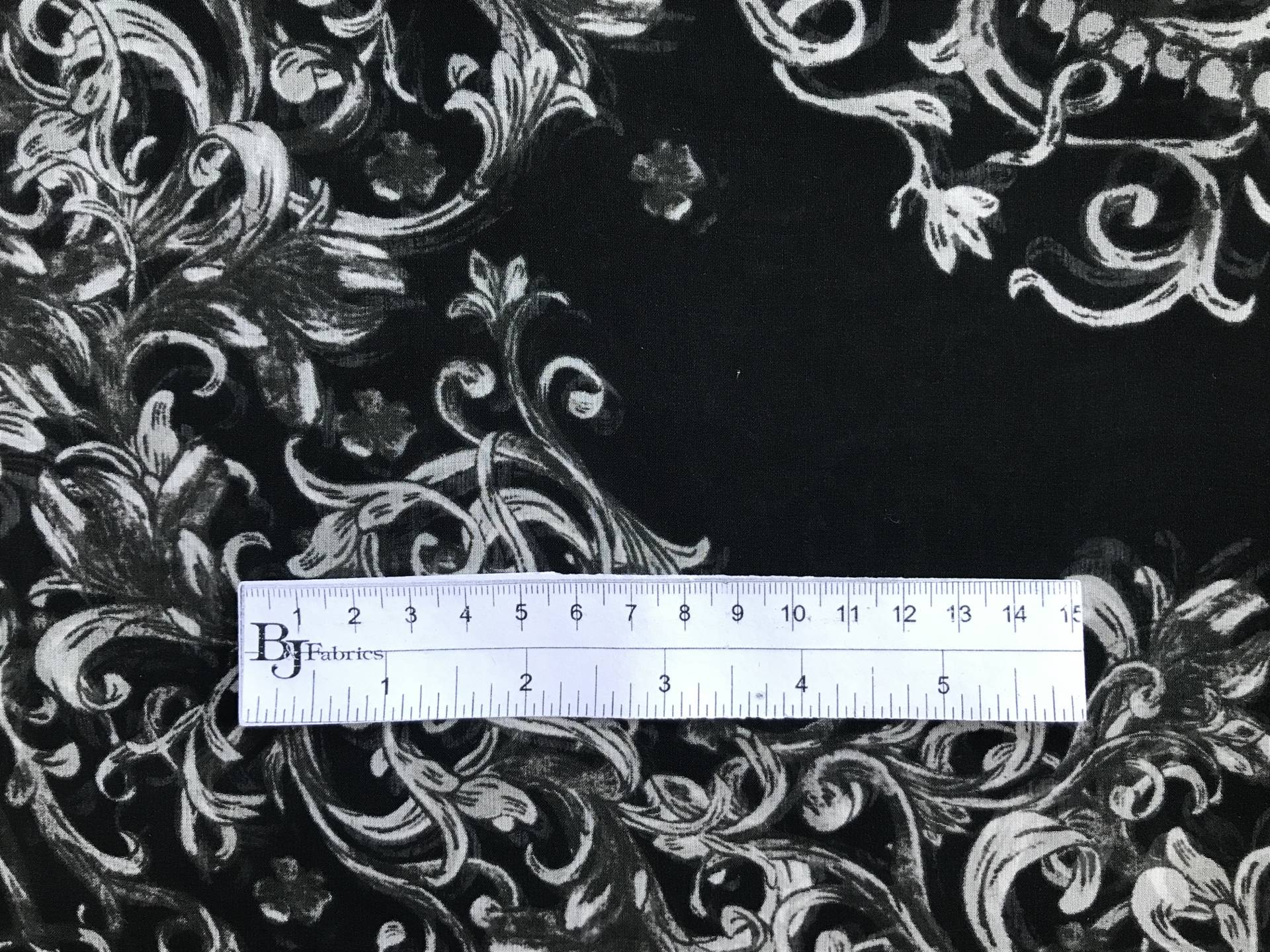 ruler sits on top of printed black chiffon with grey ornamental brocade patterns to show scale of print