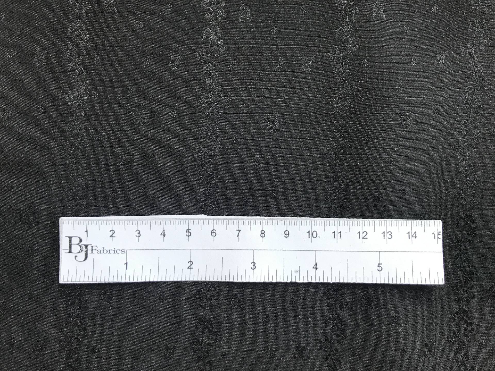ruler sits on top of black silk jacquard with rows of vines and florals to show scale of pattern