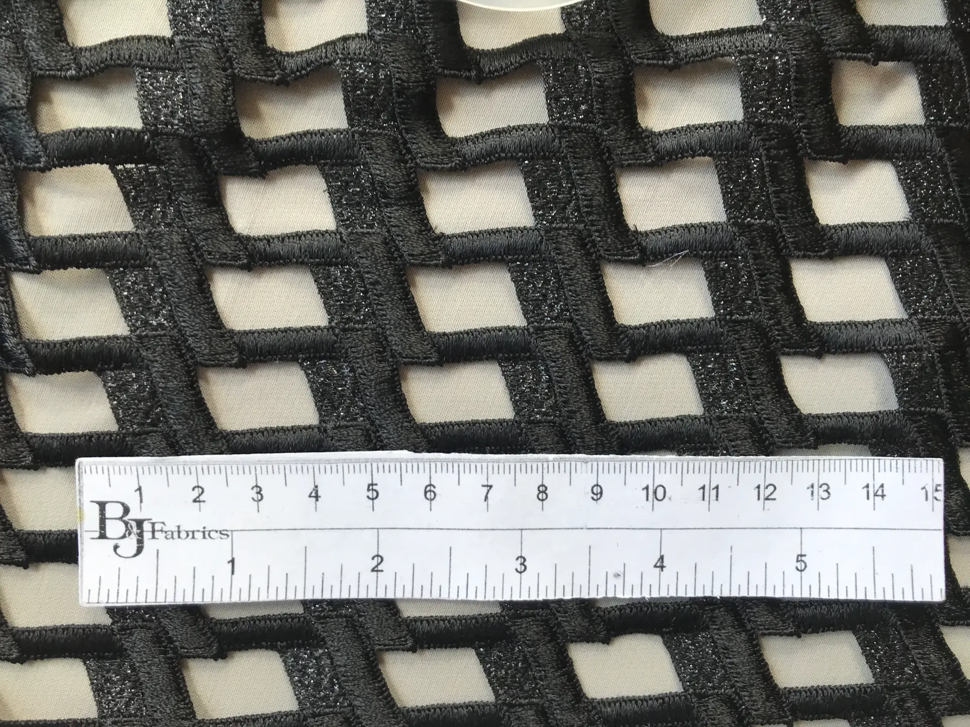 ruler sits on top of black metallic guipure lace to show scale of mesh