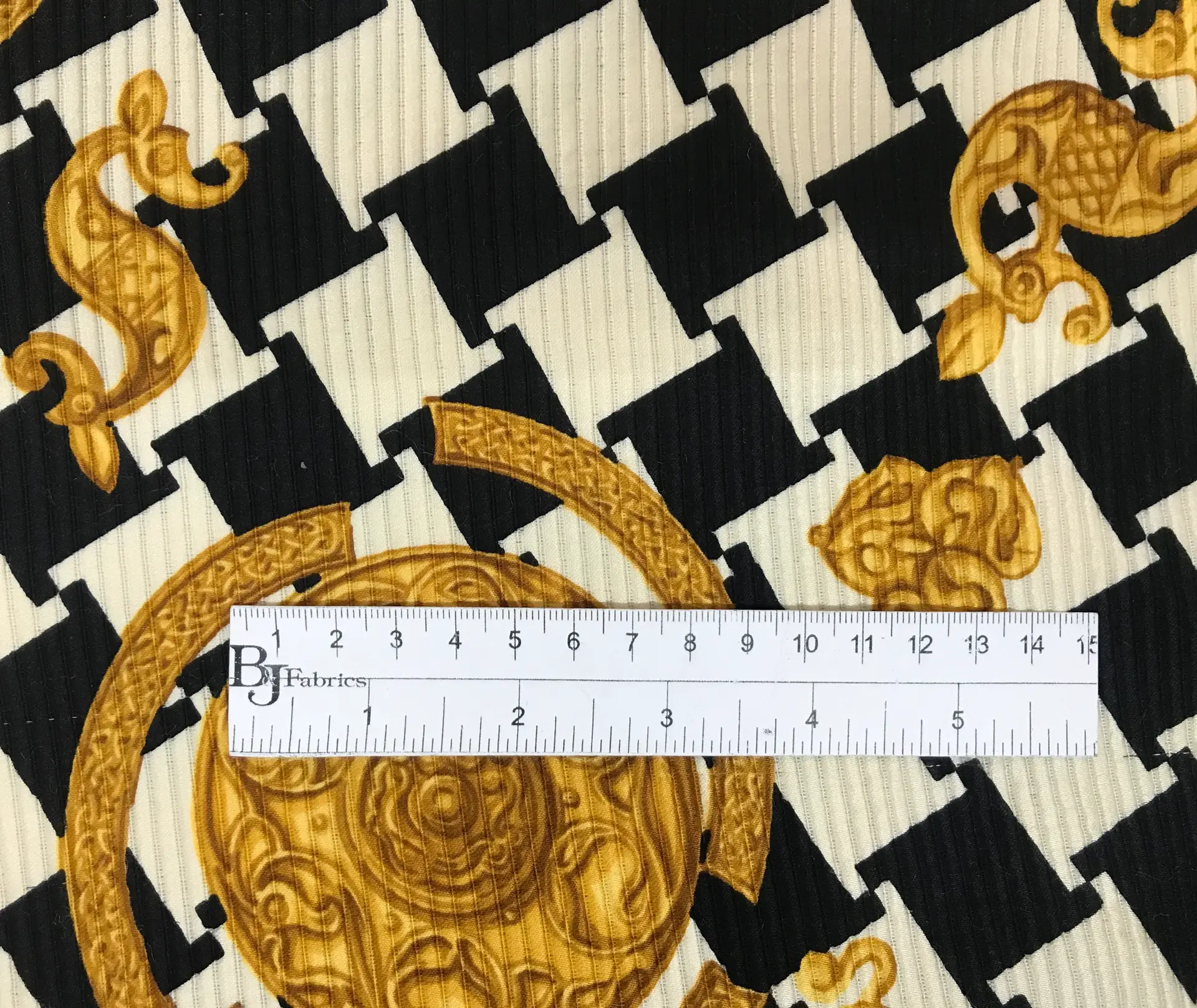 silk and wool printed ottoman, black and white abstract houndstooth and gold trinkets with ruler for scale