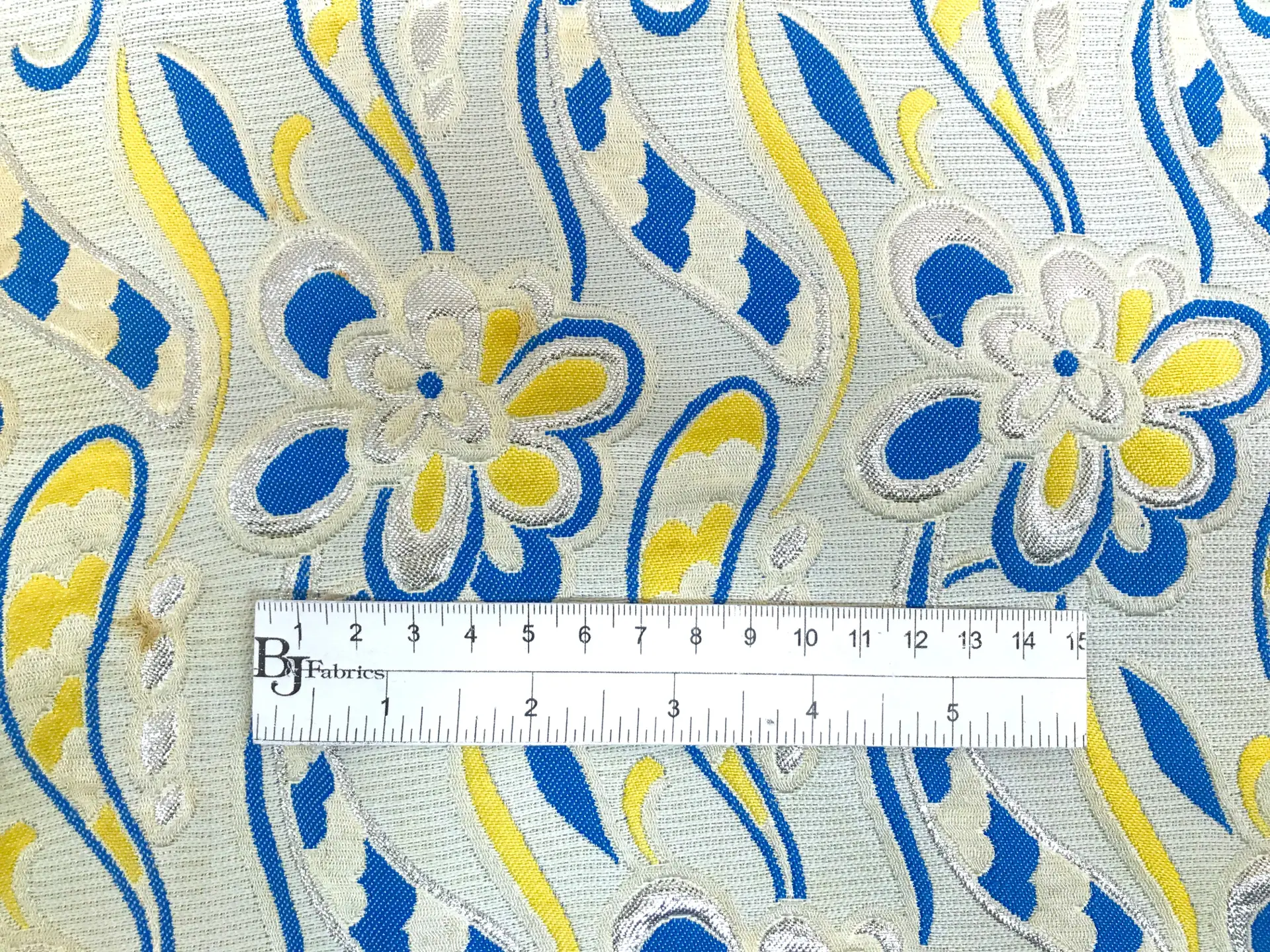 vintage brocade with 60s-esque florals in silver, yellow, and blue with ruler to show scale